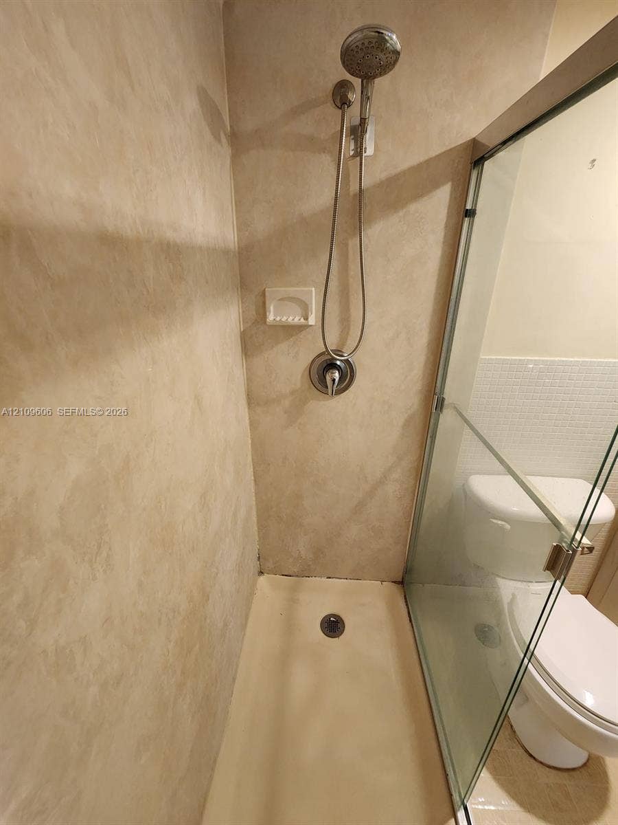 1851 NE 62nd Street, #610, Fort Lauderdale, FL 33308 Walk-in shower enclosure with beige wall surround, integrated soap niche, handheld showerhead fixture, and glass door panel
