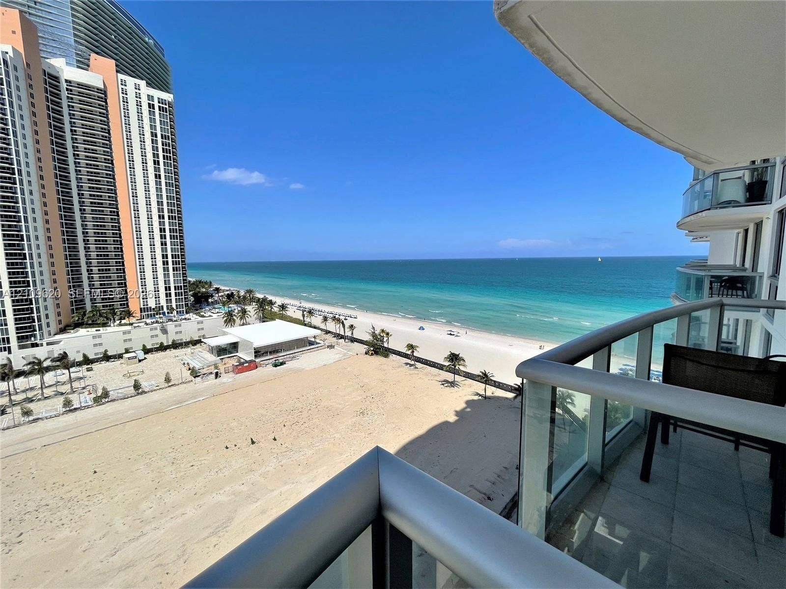 Private balcony featuring metal railings, glass panels, and tile flooring, oriented toward the coastline and ocean