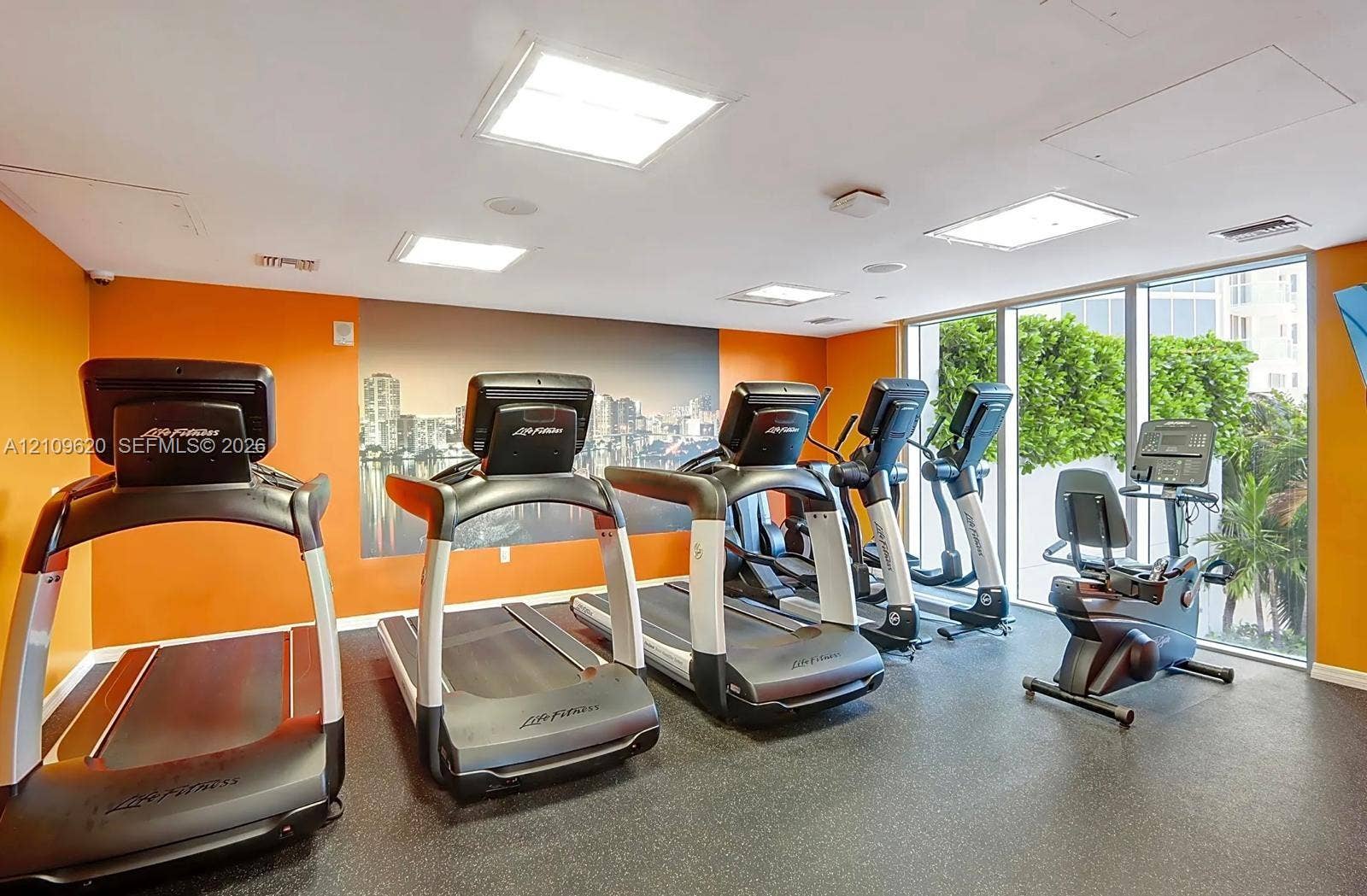 Fitness center featuring impact-resistant rubber flooring, recessed LED panel lighting, and floor-to-ceiling windows