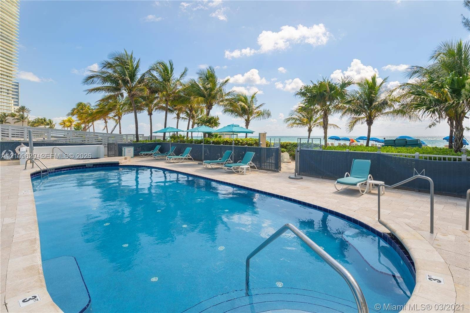 Swimming pool with stone-tiled decking, metal safety railings, and perimeter fencing