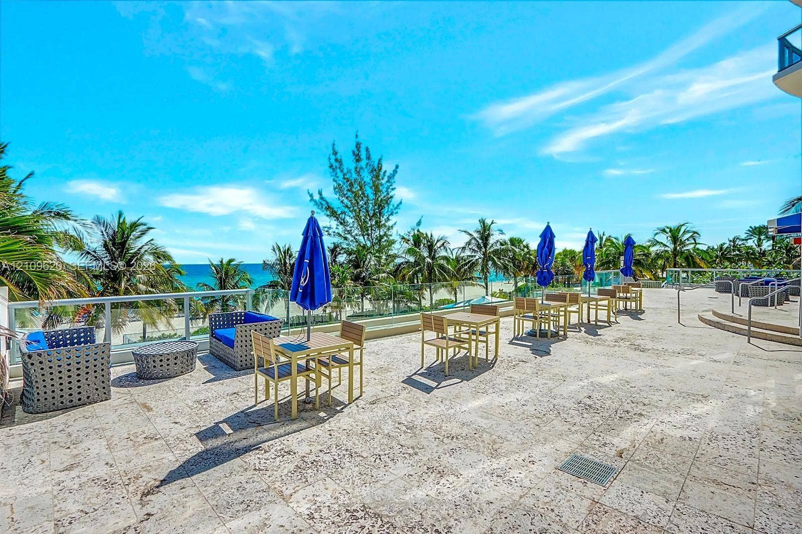 Expansive stone-paved terrace featuring a glass panel perimeter railing and mature palm trees