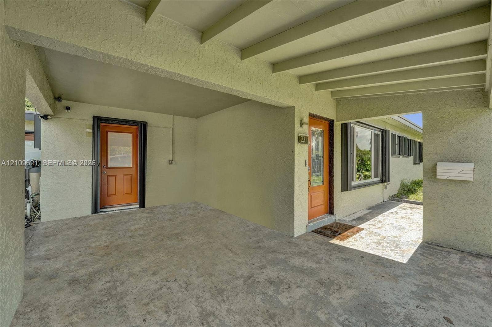 231 SW 64th Way, Pembroke Pines, FL 33023 Covered carport with exposed beam ceiling, stucco exterior walls, two solid-core doors with glass inserts, and concrete flooring