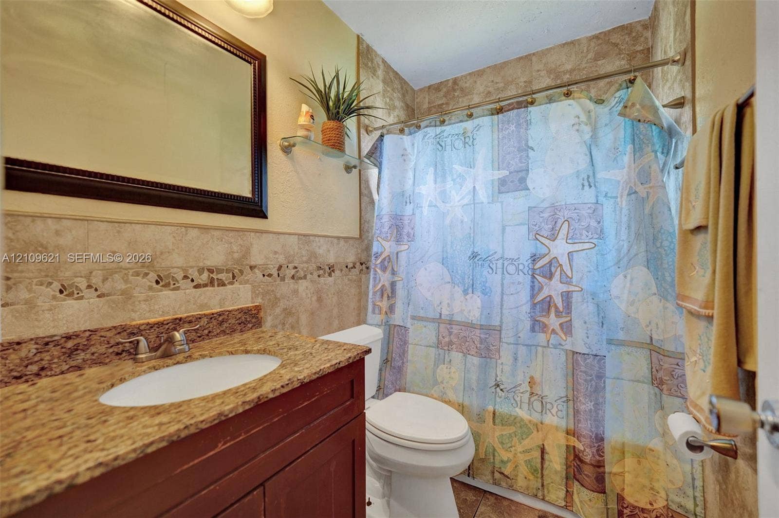 231 SW 64th Way, Pembroke Pines, FL 33023 Bathroom featuring a stone-finish countertop with an integrated oval basin, dark wood-finish vanity cabinetry, full-wall tiling with decorative inlay, and a wall-mounted mirror