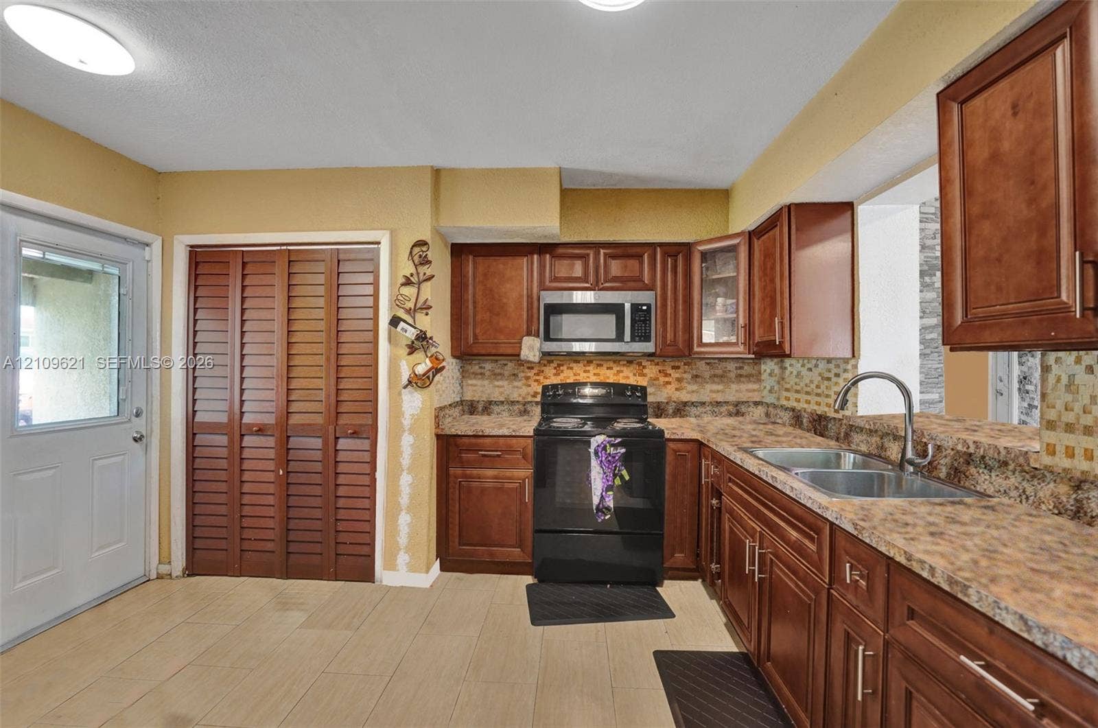 231 SW 64th Way, Pembroke Pines, FL 33023 Kitchen featuring wood cabinetry, stone-pattern laminate countertops, tiled backsplash, stainless steel microwave, and dual-basin stainless steel sink