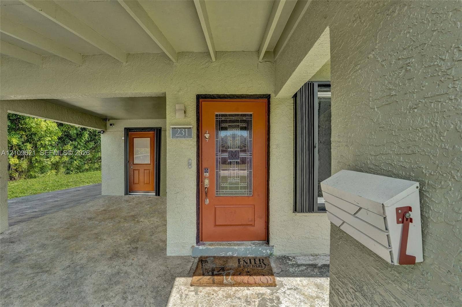 231 SW 64th Way, Pembroke Pines, FL 33023 Covered entryway featuring a textured exterior finish, two distinct orange doors with decorative glass inserts, and a wall-mounted metal mailbox