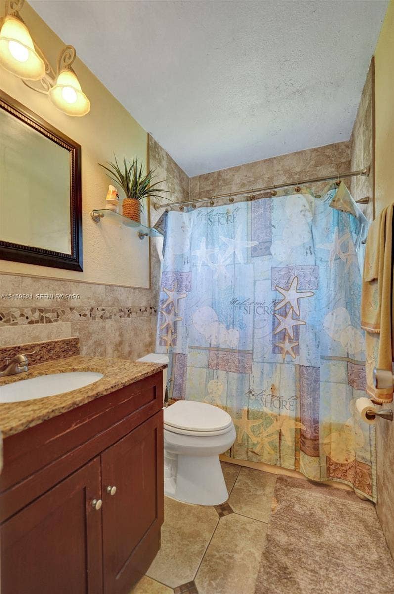 231 SW 64th Way, Pembroke Pines, FL 33023 Bathroom featuring a vanity with stone-finish countertop, integrated sink, wall-mounted lighting, tile flooring, and a tile-surround tub enclosure