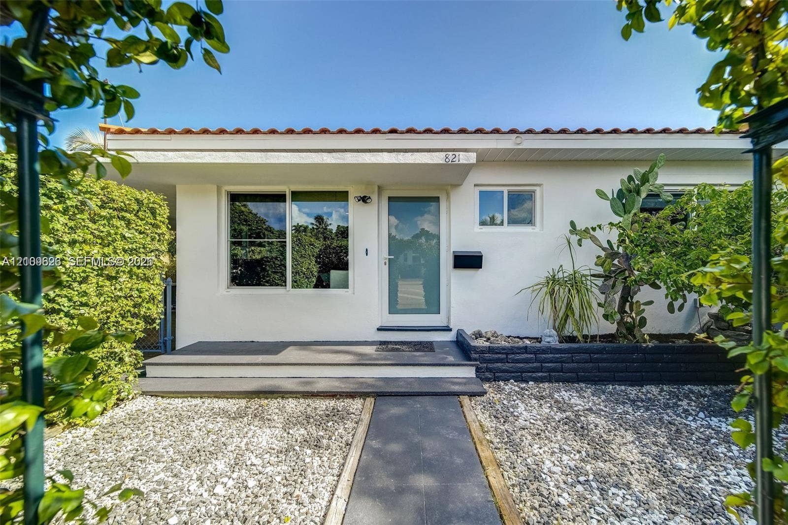 Single-story exterior featuring a low-pitch tile roof, painted stucco siding, a glass-panel entry door, and a raised concrete porch with a central walkway