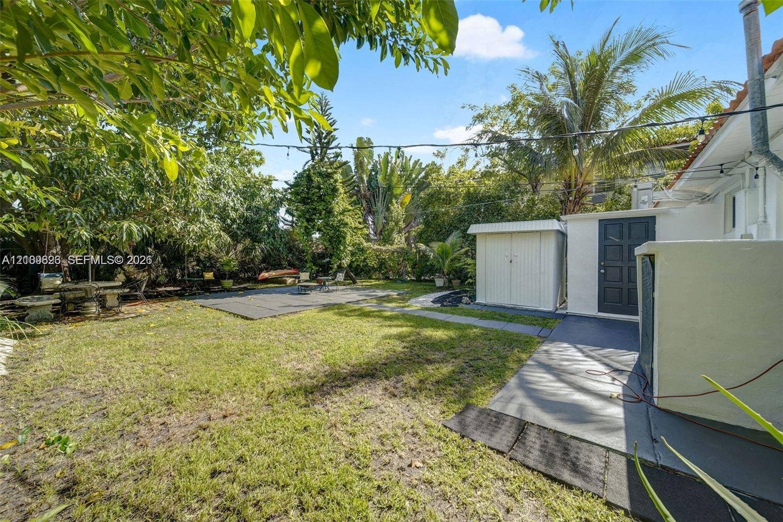 Rear yard featuring a lawn, paved patio area, detached storage structure, and mature perimeter landscaping