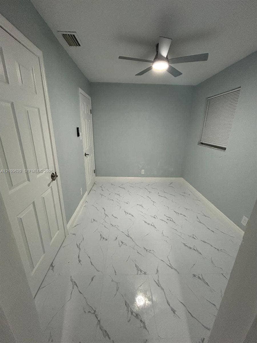 1741 NW 24th Terrace, Fort Lauderdale, FL 33311 Room featuring polished, marble-patterned tile flooring, neutral wall paint, white six-panel interior doors, and a ceiling-mounted light fixture with integrated fan