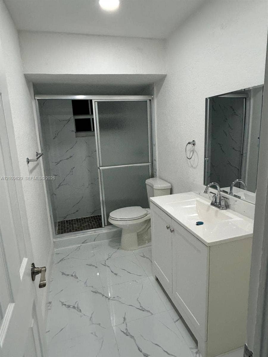 1741 NW 24th Terrace, Fort Lauderdale, FL 33311 Bathroom featuring white cabinetry with integrated countertop, polished large-format tile flooring, shower enclosure with glass doors, and decorative wall tiling
