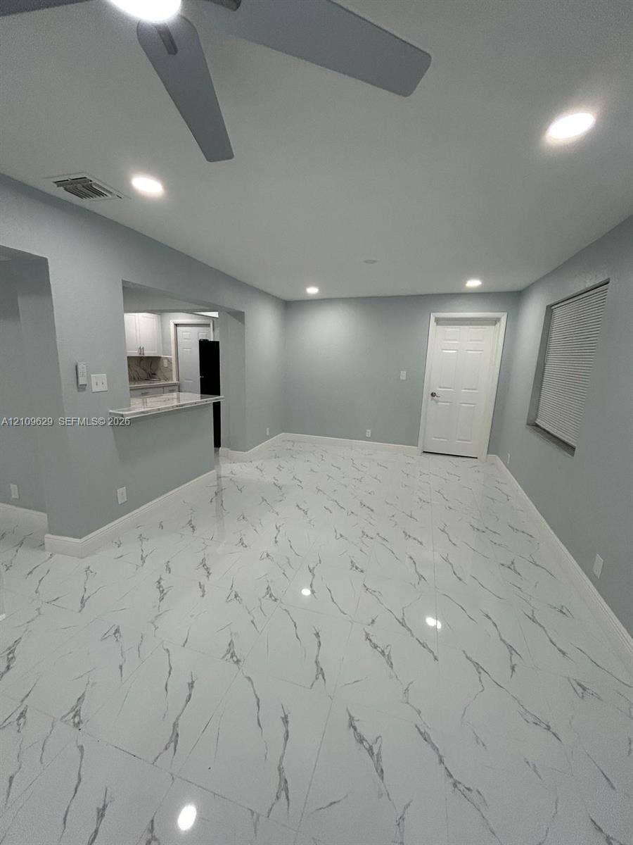 1741 NW 24th Terrace, Fort Lauderdale, FL 33311 Polished tile flooring with high-contrast veining, recessed lighting, ceiling fan, and a pass-through breakfast bar featuring stone-surface countertop