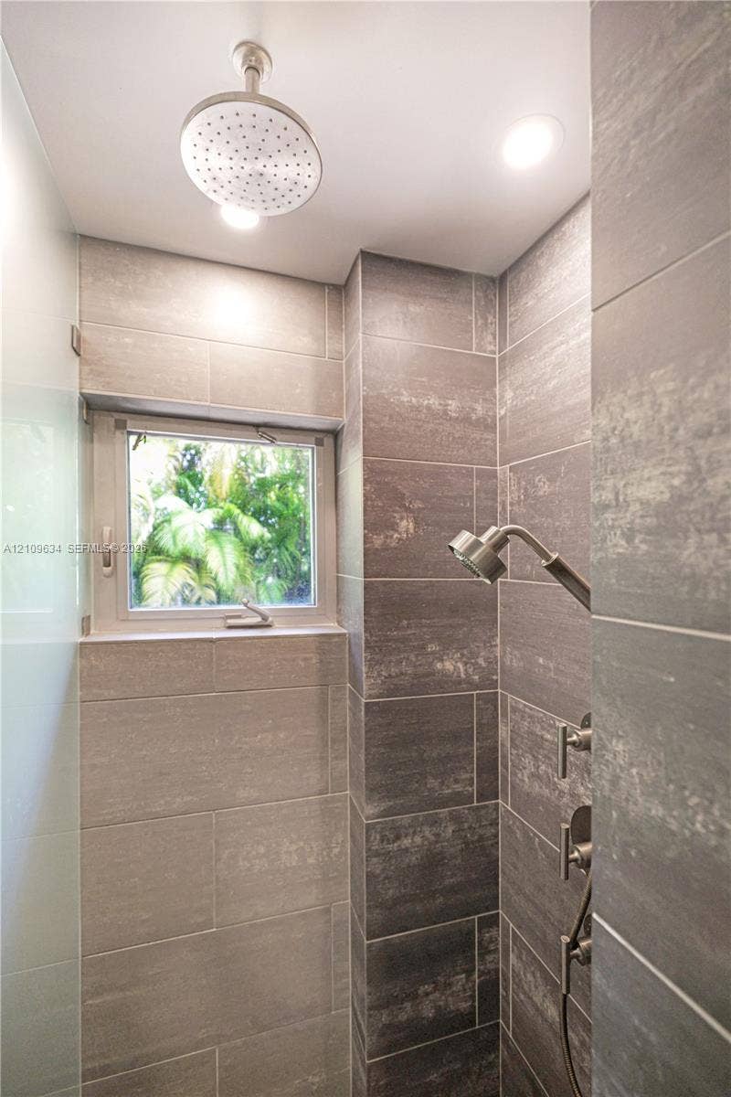 Shower enclosure featuring floor-to-ceiling large-format tile, ceiling-mounted rainfall showerhead, adjustable handheld shower fixture, and built-in window