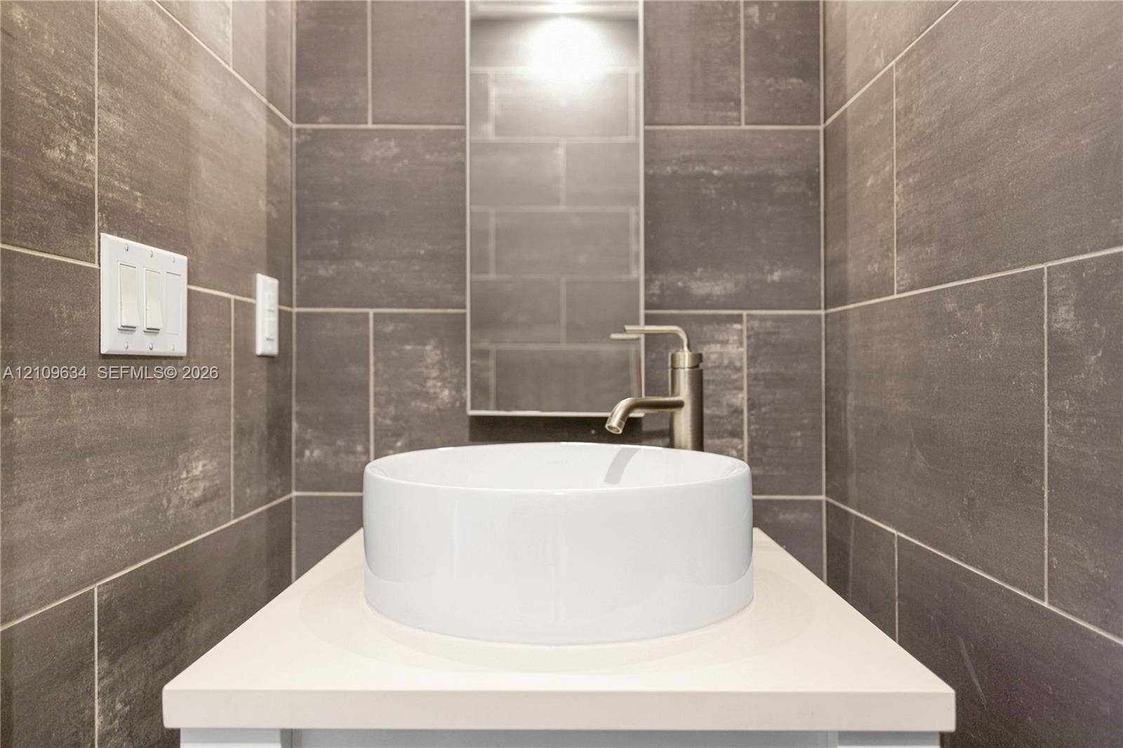 Rectangular vanity featuring a solid surface countertop, white ceramic vessel sink, brushed-finish faucet, and full-height wall tiling
