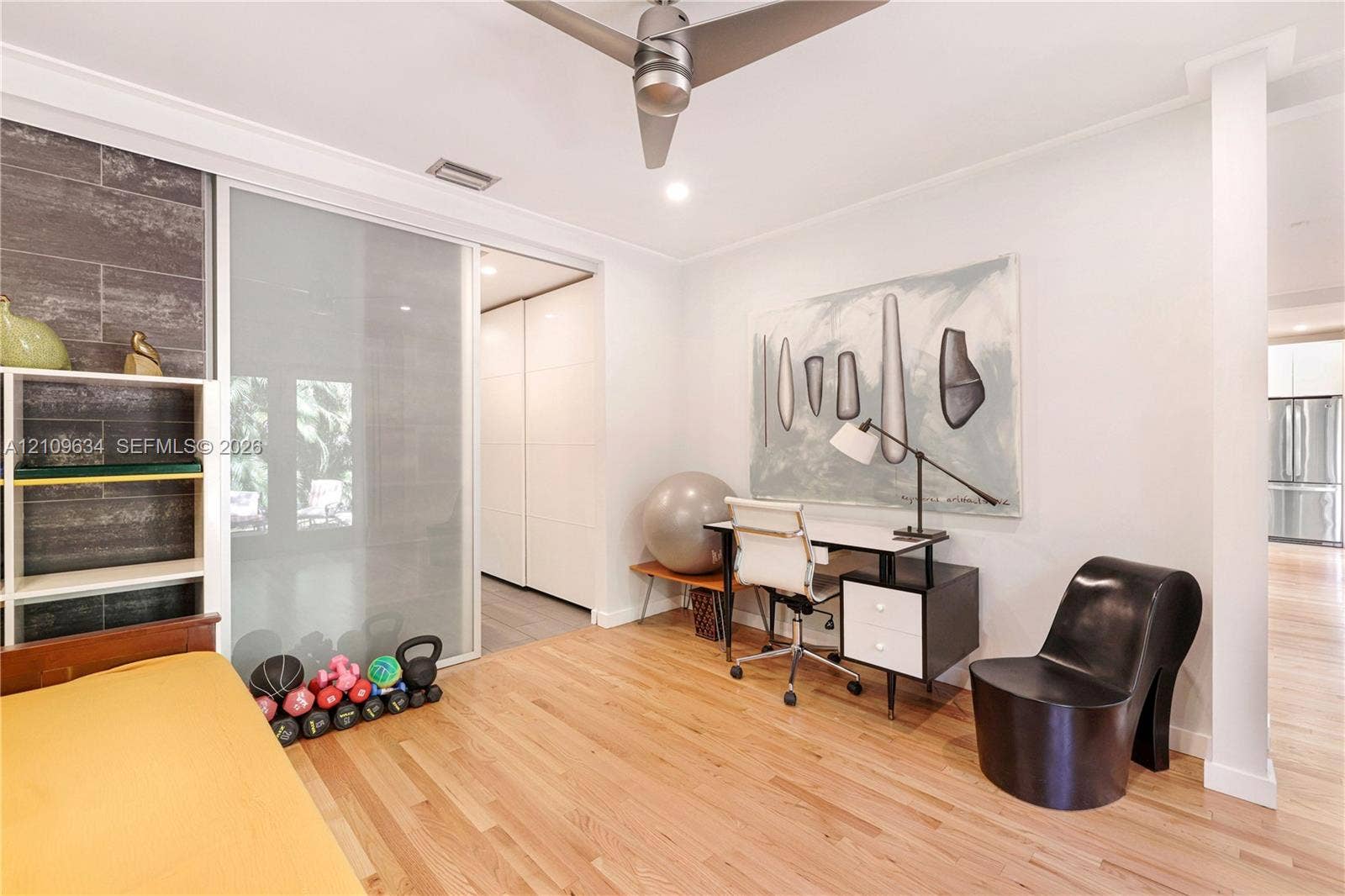 Wood-finish flooring, matte metallic ceiling fan, frosted glass sliding partition, and large-format tile accent wall