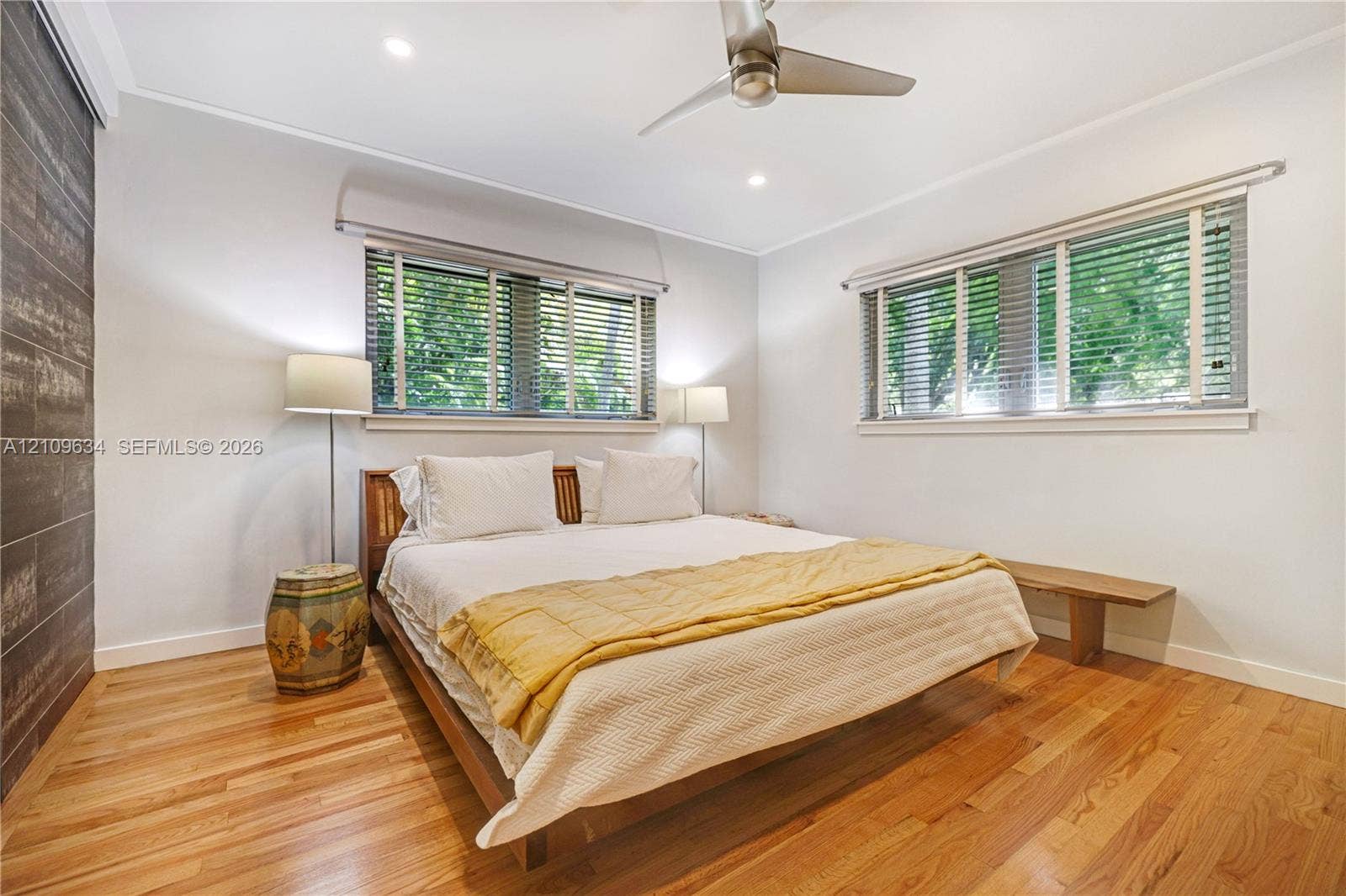 Hardwood flooring, accent wall with tile finish, dual windows with horizontal blinds, and ceiling fan