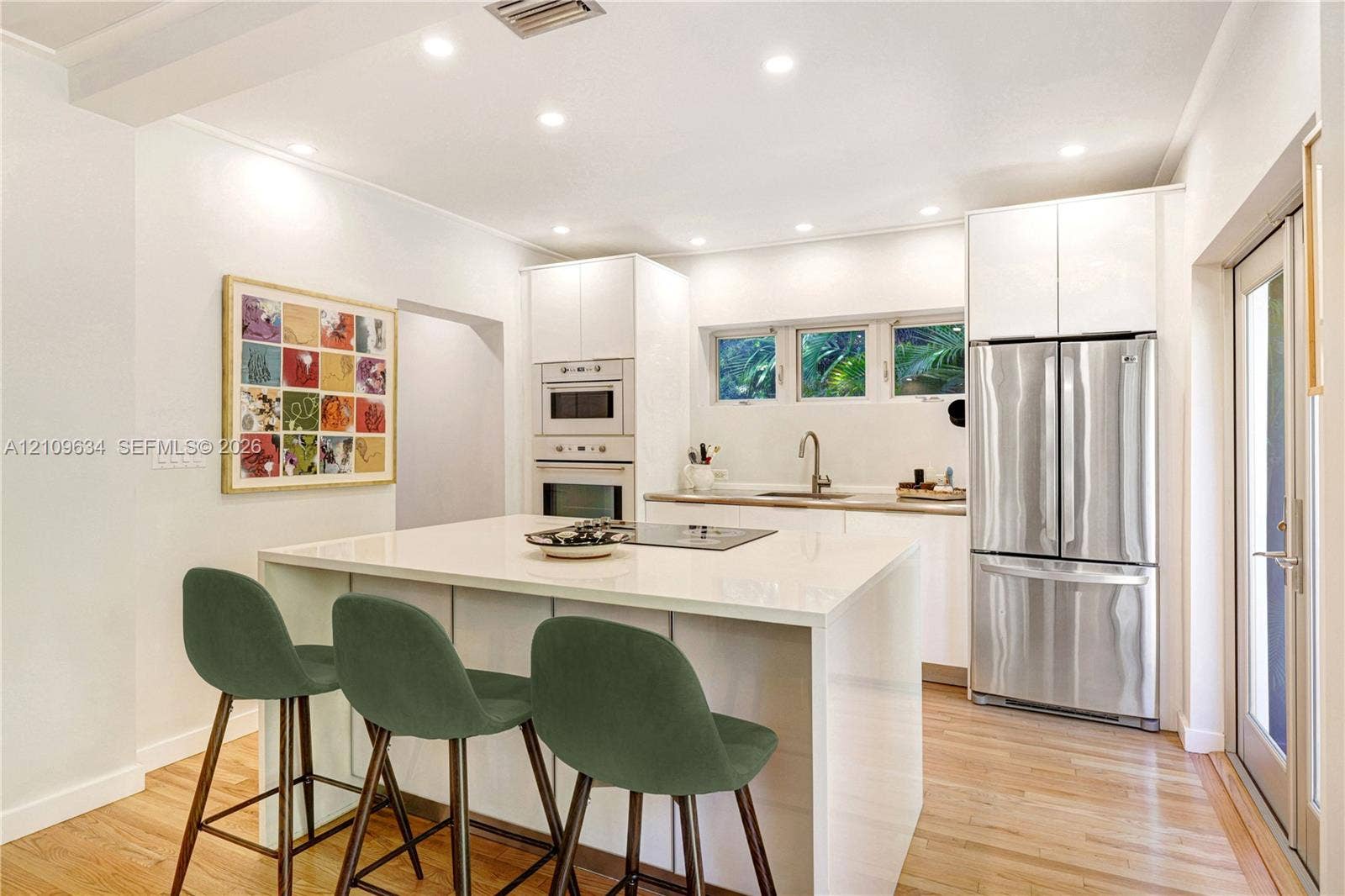 Kitchen featuring white flat-panel cabinetry, a central island with a solid-surface countertop, built-in stainless steel double wall ovens, recessed lighting, and wood-finish flooring