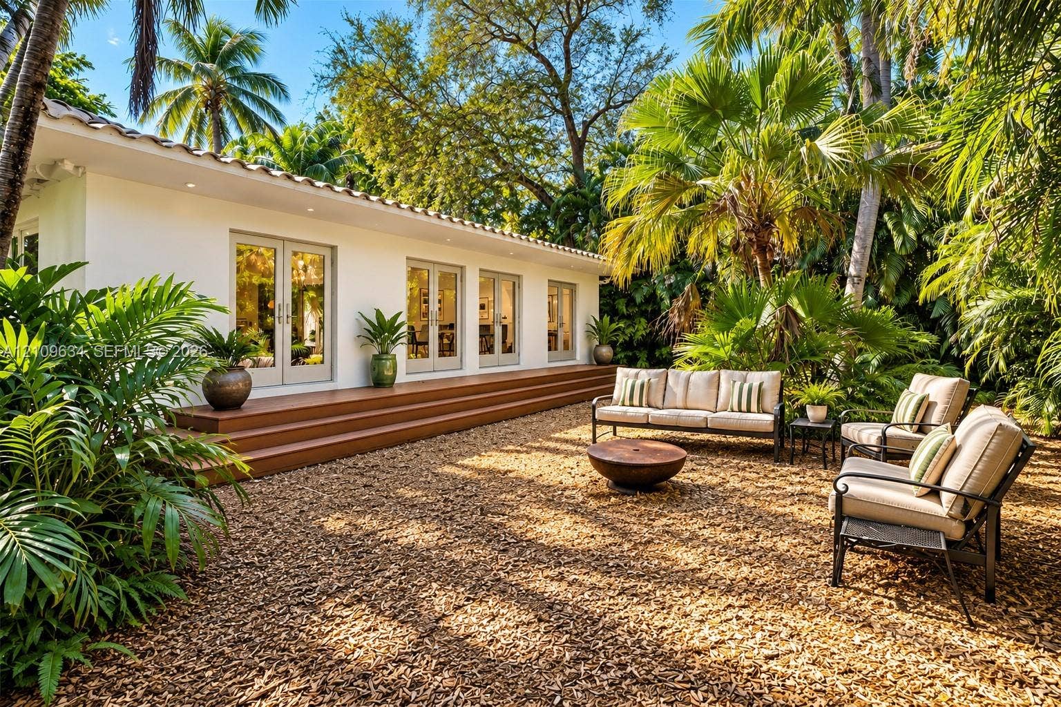 Exterior space featuring a wood-finish deck, multiple sets of glass-paneled double doors, stucco siding, and mature perimeter landscaping