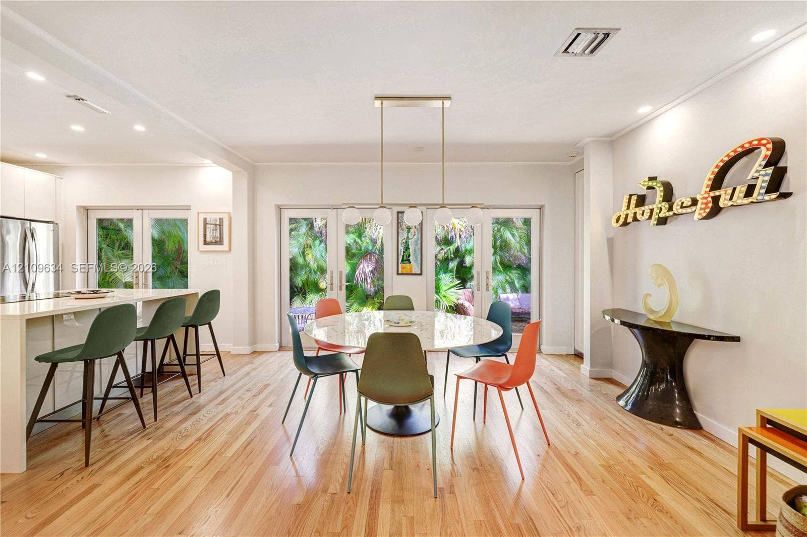 Open-concept living space featuring wood-finish flooring, recessed lighting, a modern linear pendant light, a kitchen island with stone-finish countertop, and glass-paned double doors