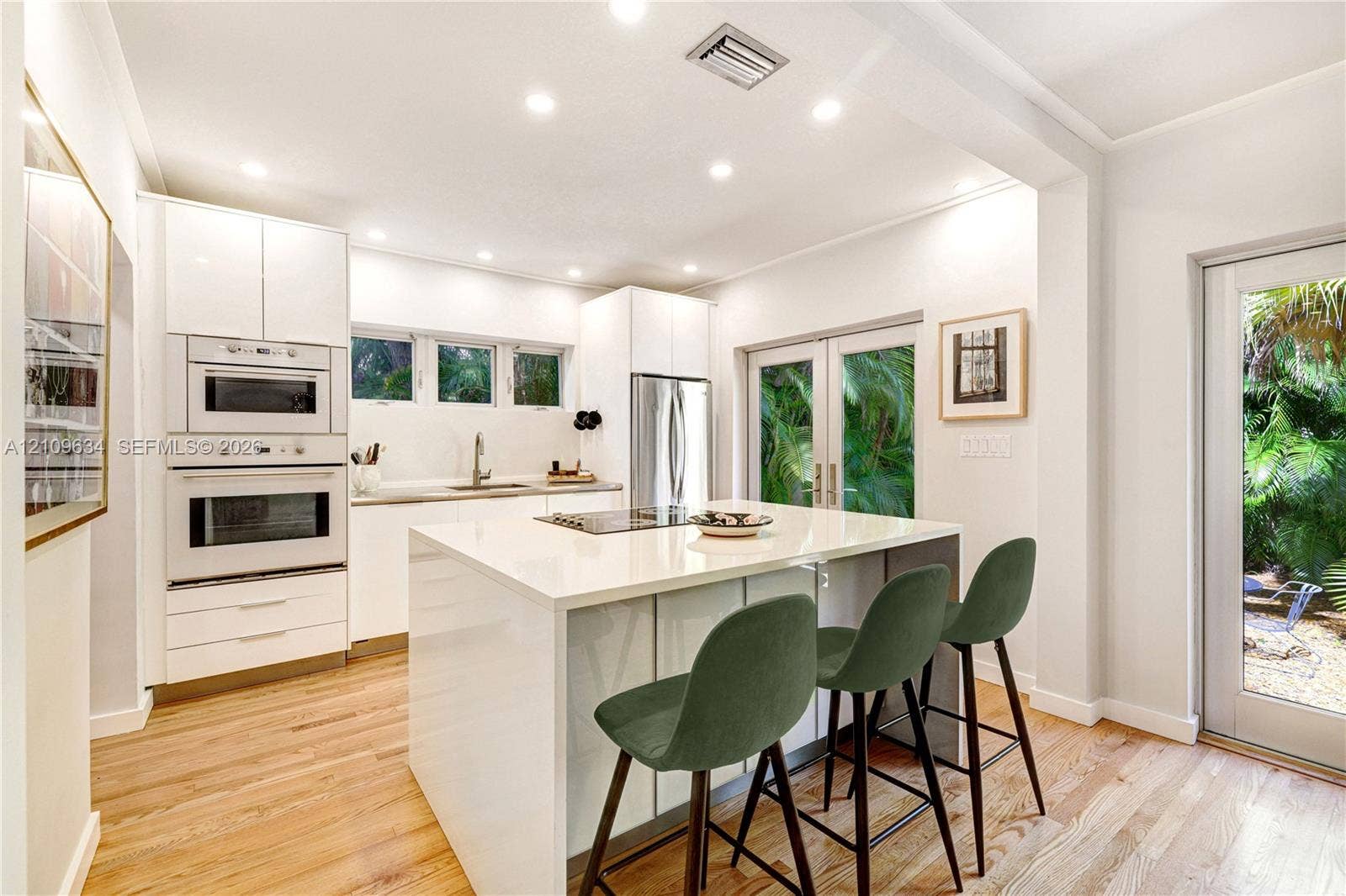 Kitchen featuring a center island with a solid-surface countertop, white flat-panel cabinetry, built-in stainless steel double ovens, wood-finish flooring, and glass-paned doors
