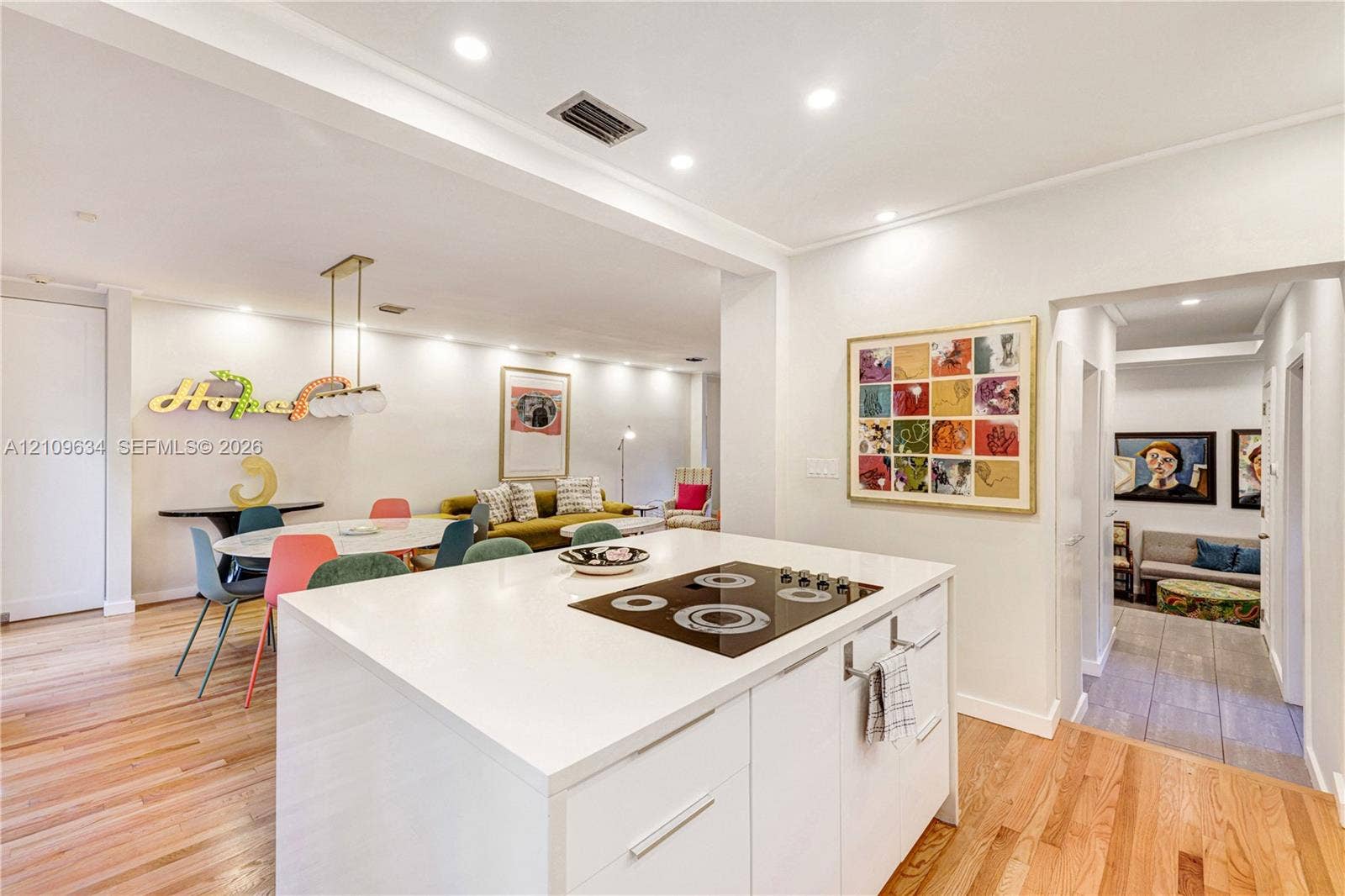 Kitchen island featuring a smooth solid-surface countertop and an integrated electric cooktop, complemented by wood-finish flooring and recessed lighting