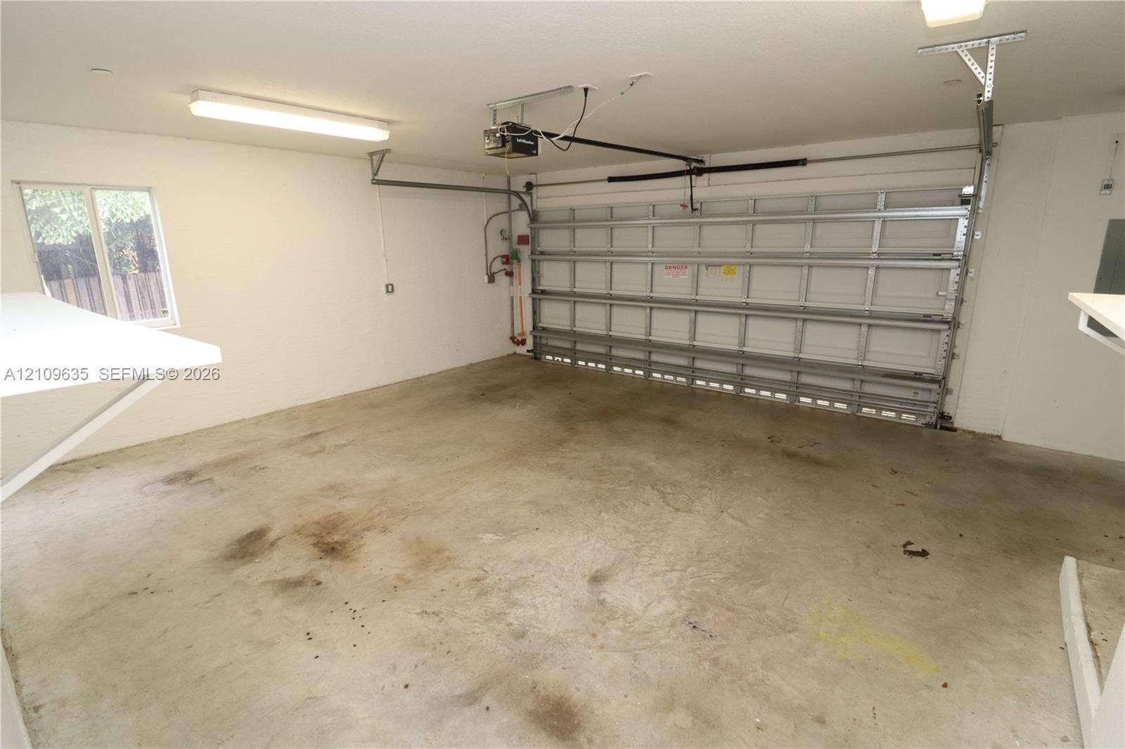 611 NE 28th Street, #1, Wilton Manors, Wilton Manors, FL 33334 Two-car garage featuring a sectional metal roll-up door, concrete flooring, overhead linear lighting, and a window