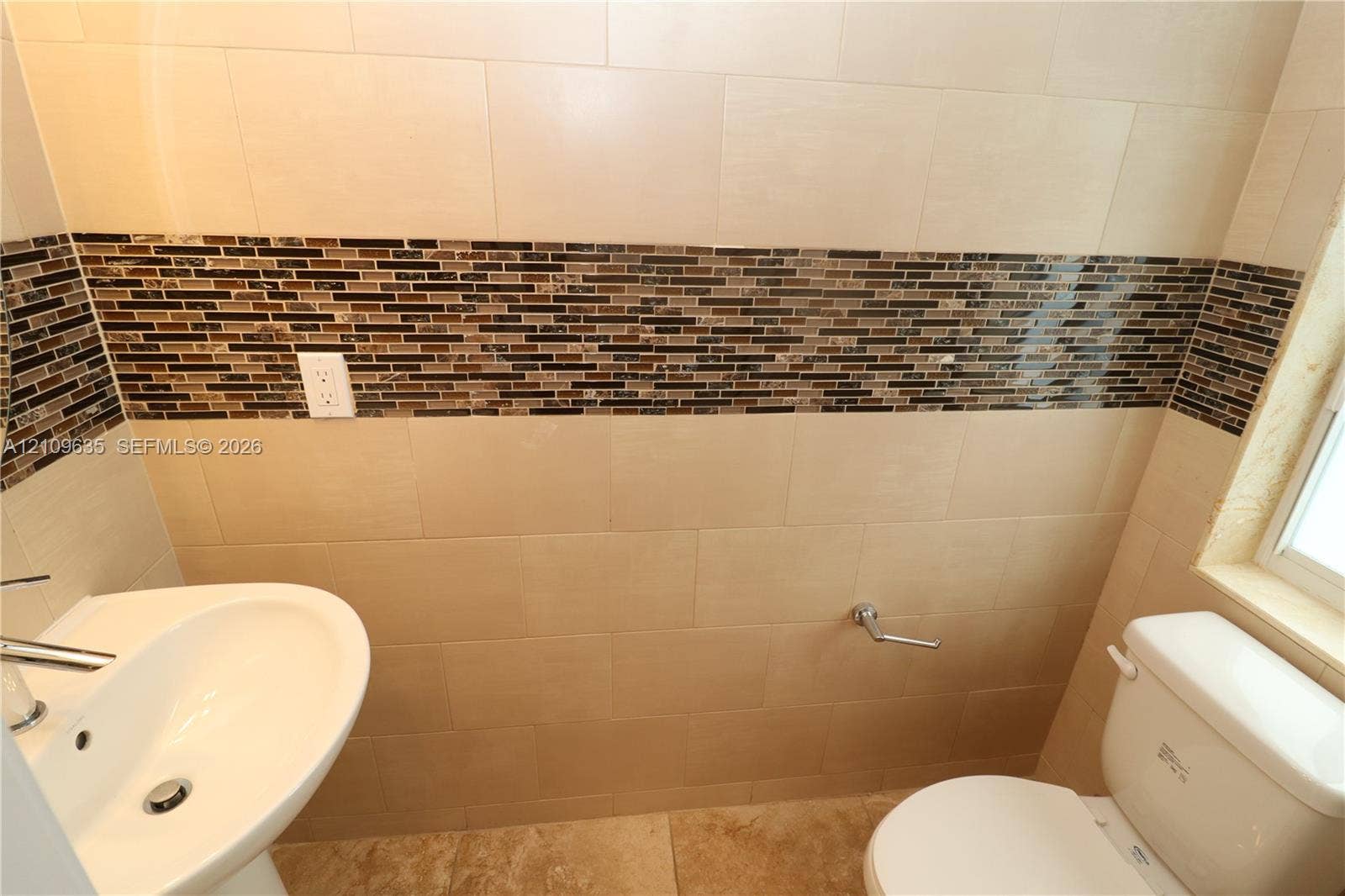 611 NE 28th Street, #1, Wilton Manors, Wilton Manors, FL 33334 Pedestal sink with chrome faucet, porcelain tile flooring, and wall surfaces featuring large-format beige tiles accented by a horizontal glass mosaic border