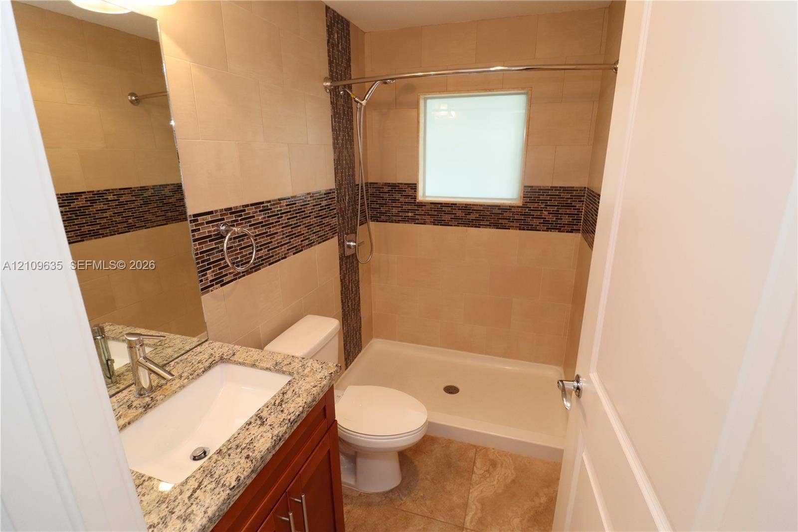 611 NE 28th Street, #1, Wilton Manors, Wilton Manors, FL 33334 Bathroom featuring stone-finish countertop with an integrated basin, wood-finish cabinetry, walk-in shower with tile surround, mosaic decorative tile accents, and neutral floor tile