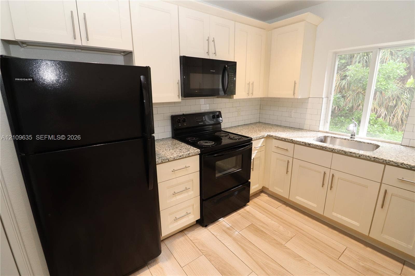 611 NE 28th Street, #1, Wilton Manors, Wilton Manors, FL 33334 Kitchen featuring off-white shaker-style cabinetry, speckled stone countertops, a white subway tile backsplash, wood-finish tile flooring, and integrated black appliances