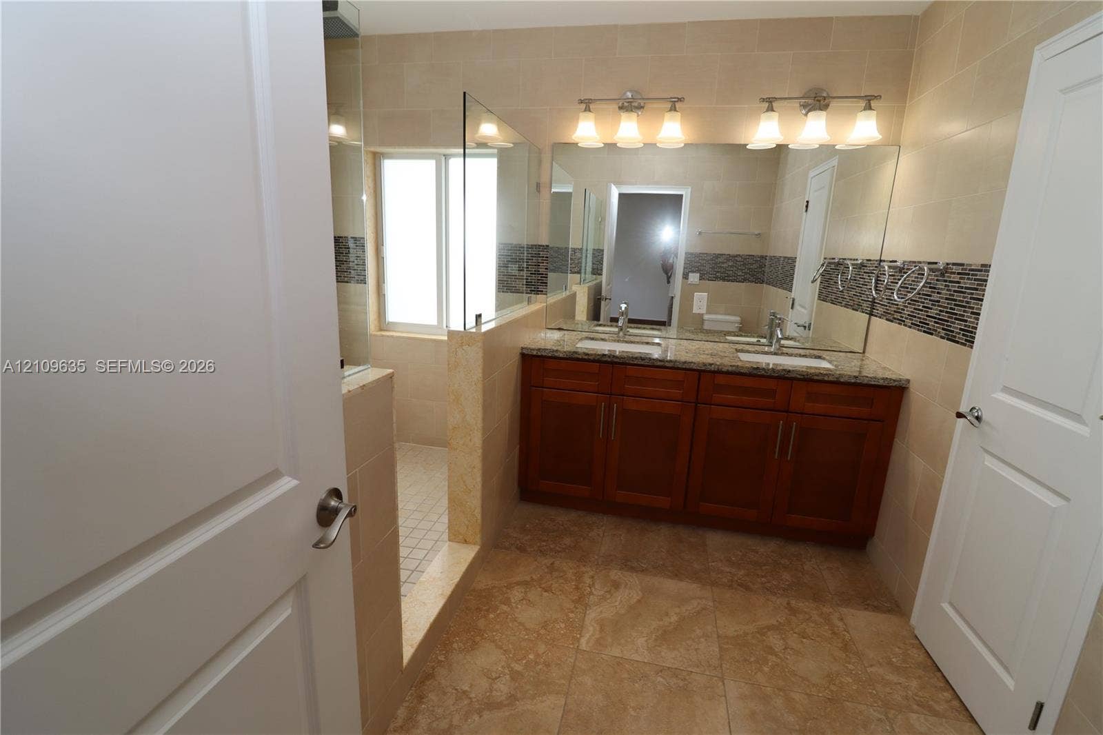 611 NE 28th Street, #1, Wilton Manors, Wilton Manors, FL 33334 Double vanity with stone-finish countertop, under-mount sinks, wood-finish cabinetry, walk-in shower with glass enclosure, and decorative tile accent wall