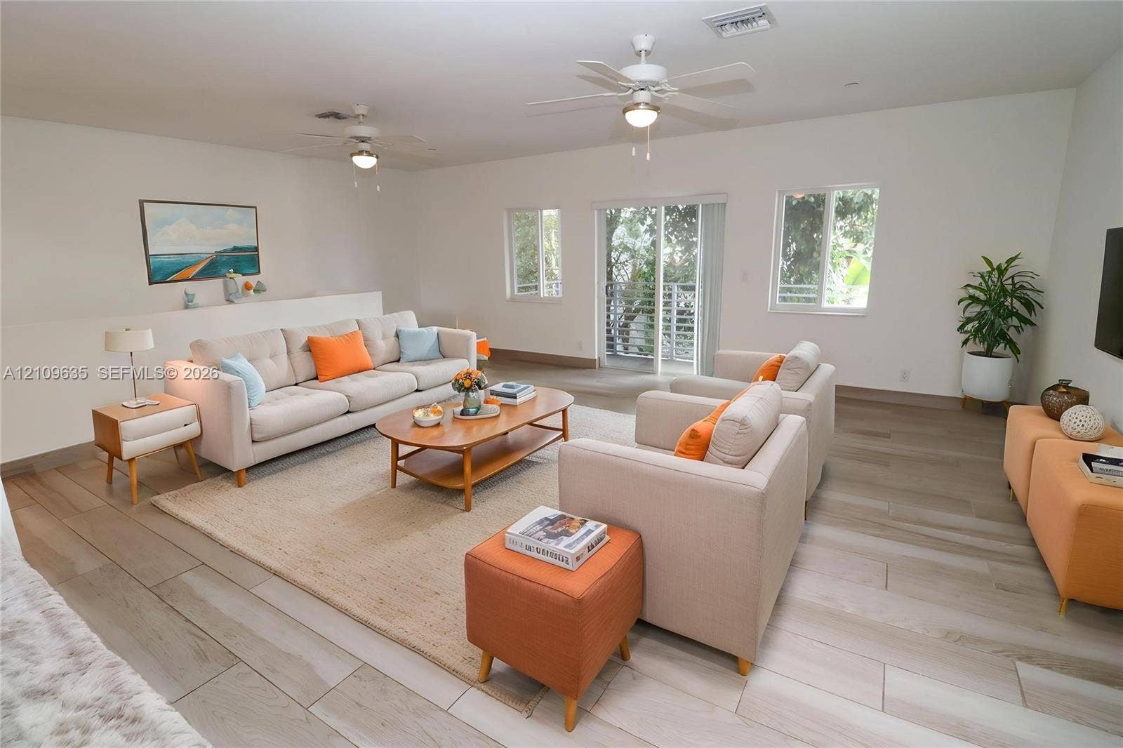 611 NE 28th Street, #1, Wilton Manors, Wilton Manors, FL 33334 Living area featuring light-toned wood-finish flooring, dual ceiling fans, multiple windows, and sliding glass doors with balcony access