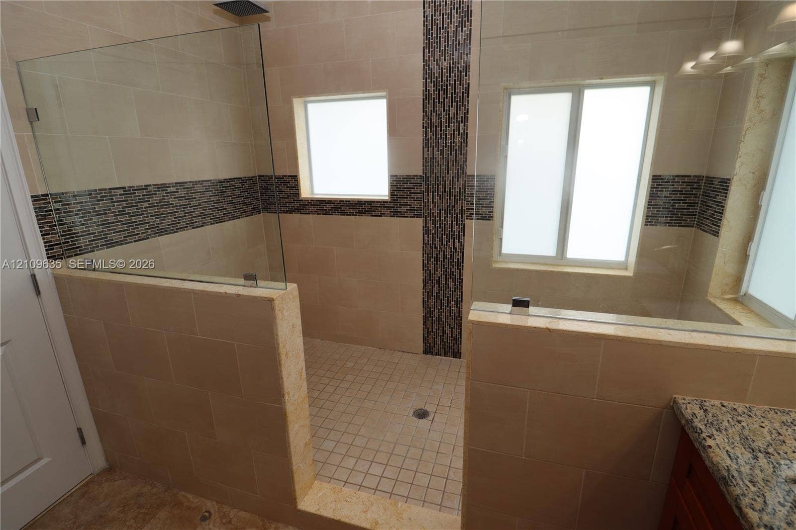 611 NE 28th Street, #1, Wilton Manors, Wilton Manors, FL 33334 Walk-in shower featuring large-format stone-look tile walls, decorative mosaic accent banding, a glass enclosure, and stone-look tile flooring