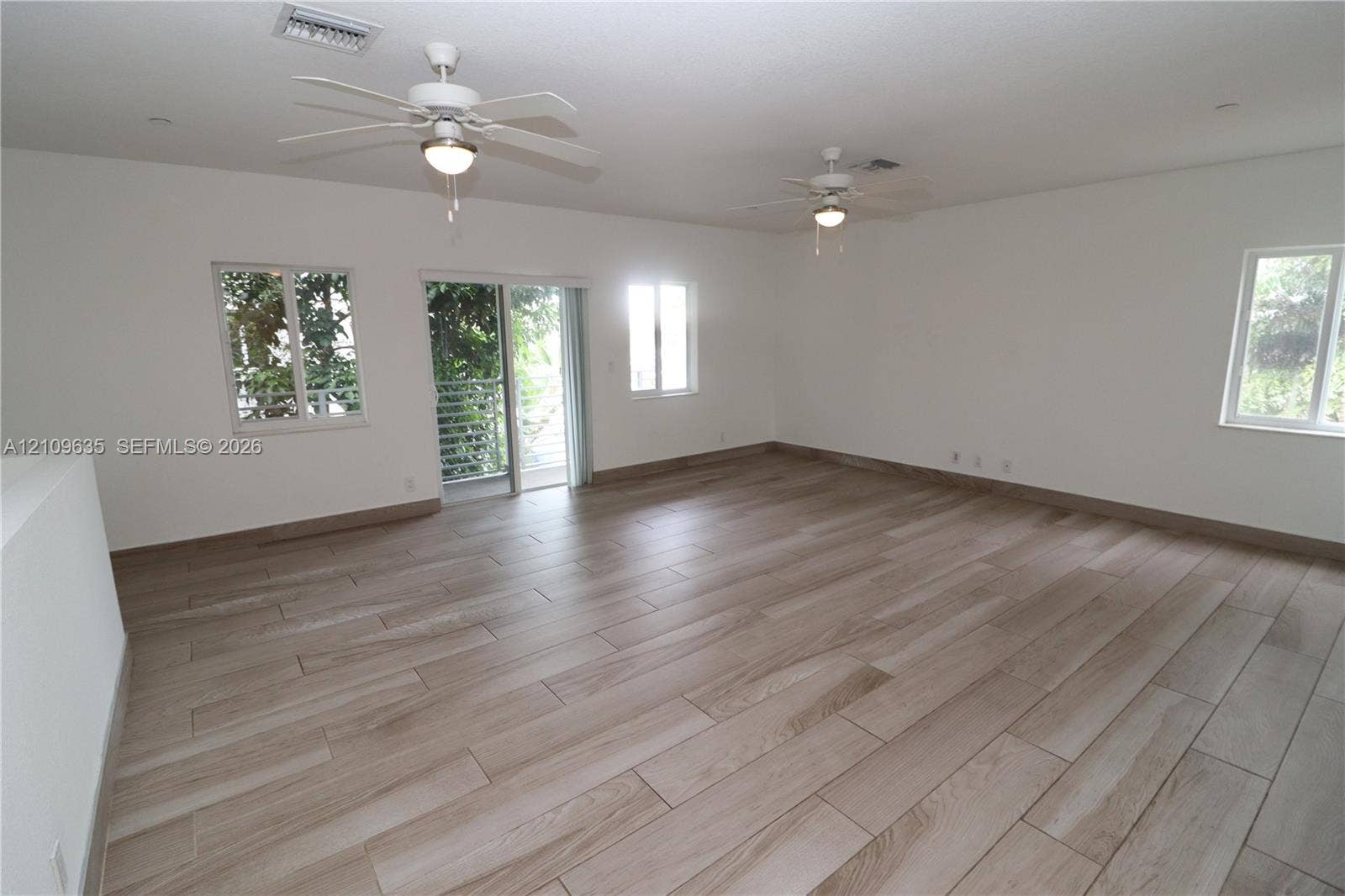 611 NE 28th Street, #1, Wilton Manors, Wilton Manors, FL 33334 Spacious interior featuring wood-finish tile flooring, dual ceiling fans, multiple windows, and a glass sliding door