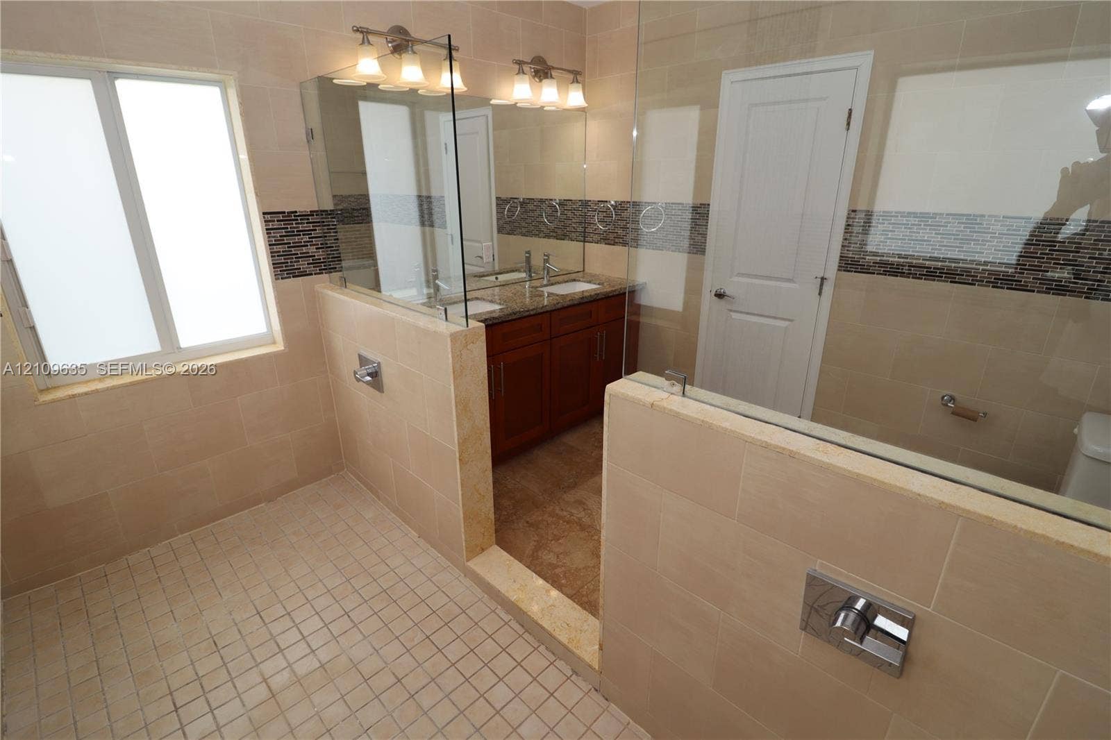 611 NE 28th Street, #1, Wilton Manors, Wilton Manors, FL 33334 Bathroom featuring a dual-sink vanity with stone countertop, frameless glass shower enclosure, large-format tile surround with glass mosaic inlay, and tile flooring