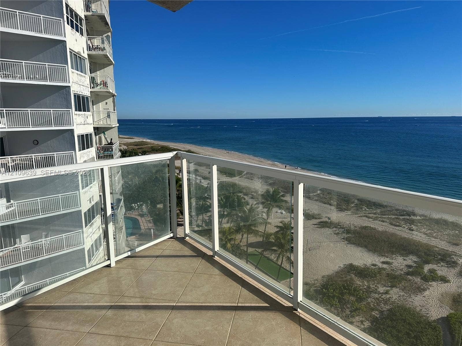 Private balcony featuring tile flooring and a glass-paneled railing overlooking the coastline