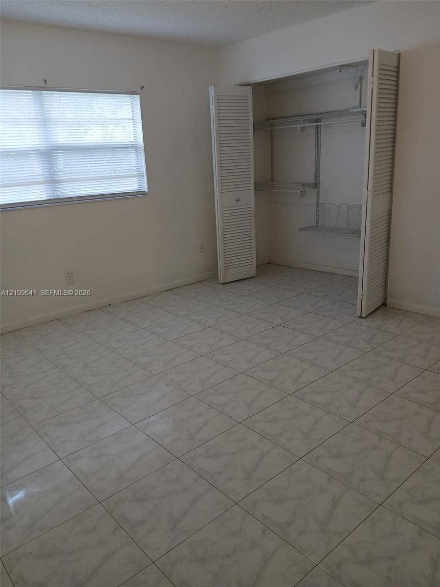 4108 NW 88th Avenue, #4, Coral Springs, Coral Springs, FL 33065 Room featuring neutral tile flooring, window with built-in blinds, and a closet with bifold louvered doors and integrated wire shelving