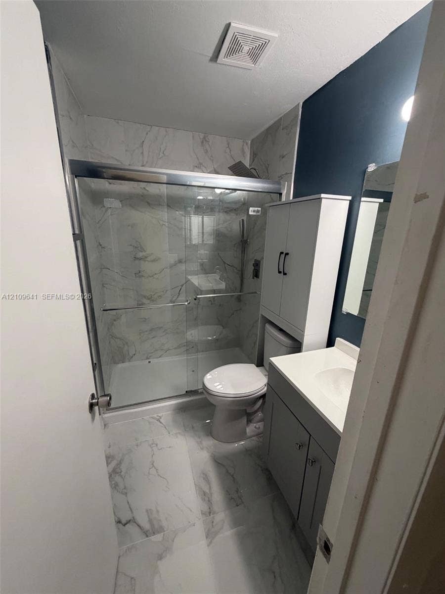 4108 NW 88th Avenue, #4, Coral Springs, Coral Springs, FL 33065 Bathroom featuring large-format stone-patterned tile flooring and wall surrounds, a glass-enclosed shower with metallic hardware, a grey vanity with a solid-surface countertop, and built-in vertical cabinetry