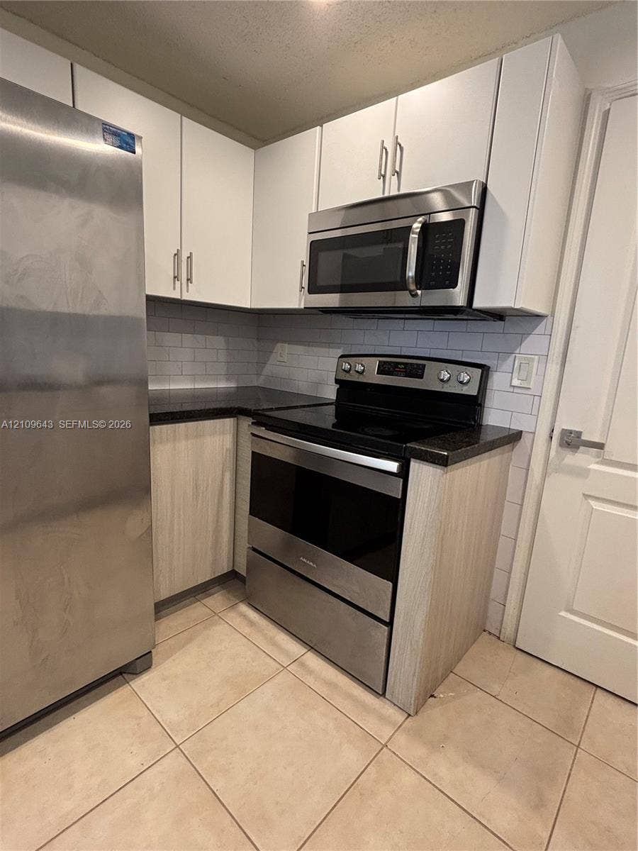 11467 NW 51st Terrace, Doral, Doral, FL 33178 Kitchen featuring stainless steel appliances, dark stone-finish countertops, subway tile backsplash, white upper cabinetry, and wood-finish lower cabinetry