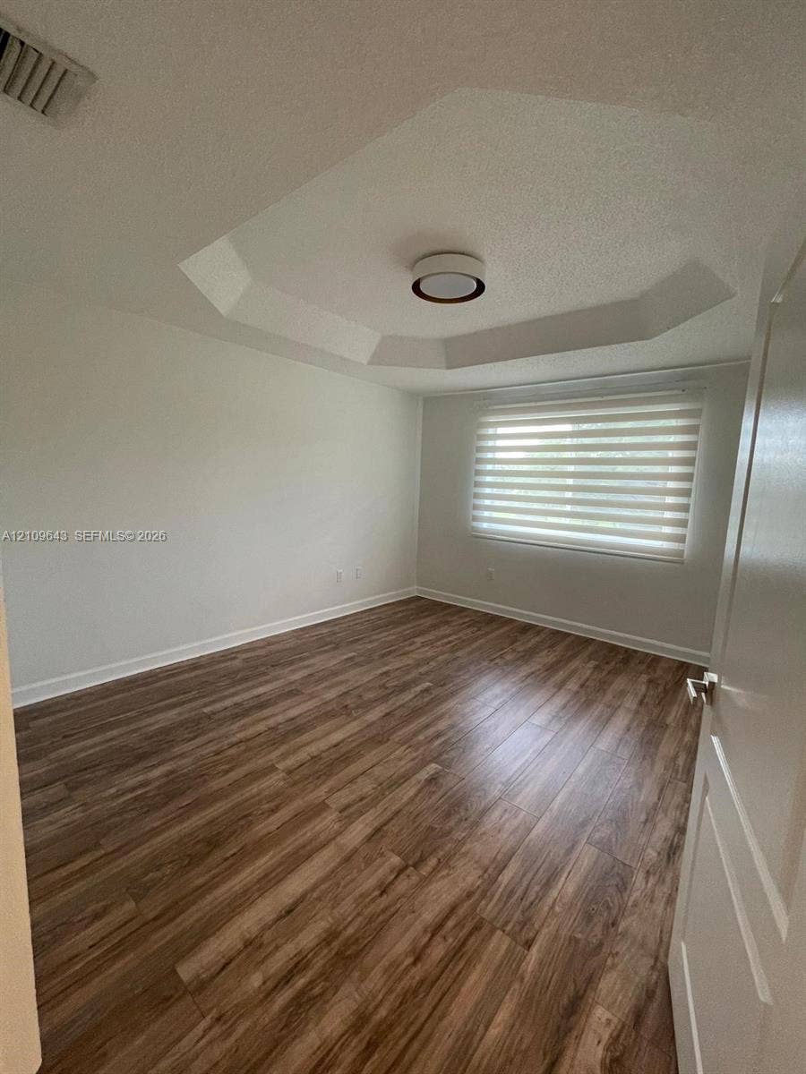 11467 NW 51st Terrace, Doral, Doral, FL 33178 Interior space featuring wood-finish flooring, a tray ceiling, flush-mount lighting, and a window with installed roller shades