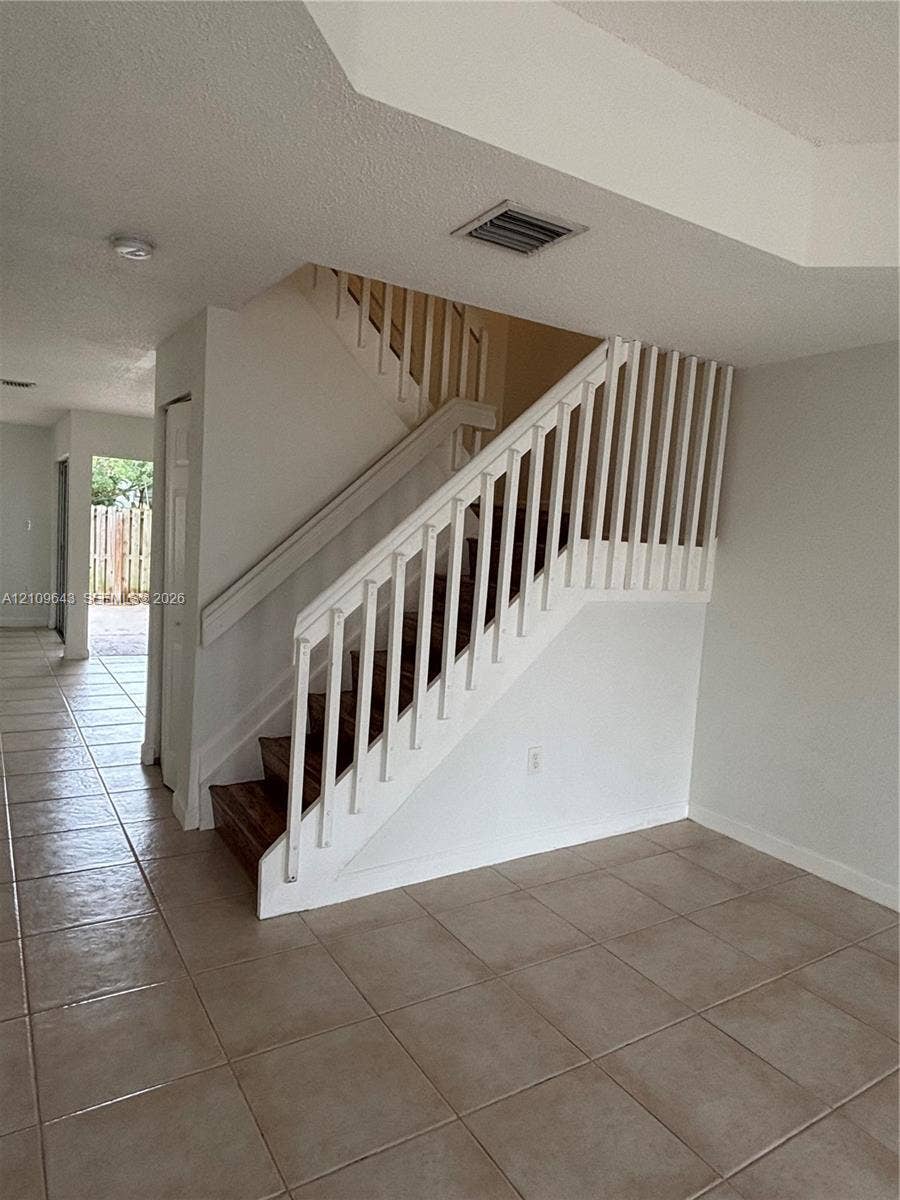11467 NW 51st Terrace, Doral, Doral, FL 33178 Staircase featuring white balusters, a wooden handrail, and wood-finish treads, complemented by neutral tile flooring throughout the open floor area