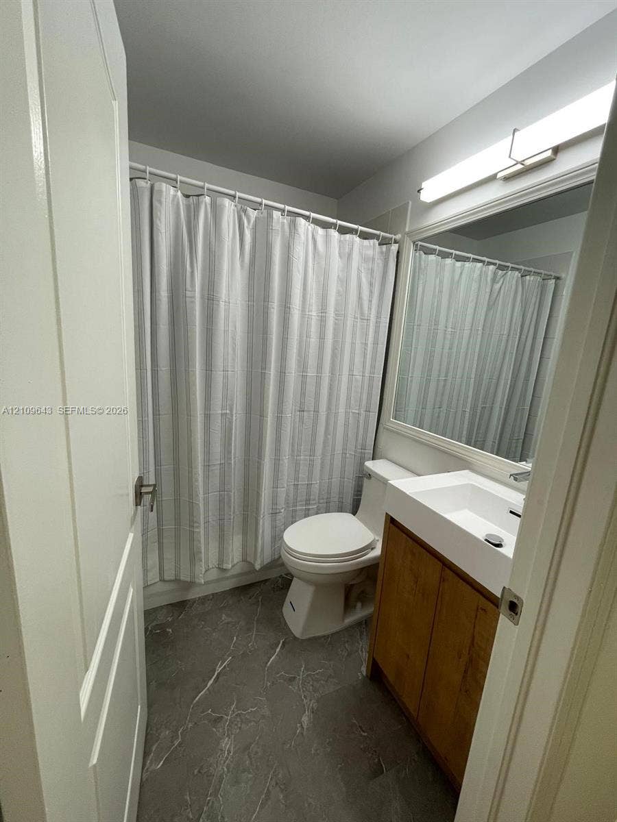 11467 NW 51st Terrace, Doral, Doral, FL 33178 Bathroom featuring a wood-finish vanity with a white rectangular sink, stone-finish flooring, a full-width mirror, and a wall-mounted light fixture