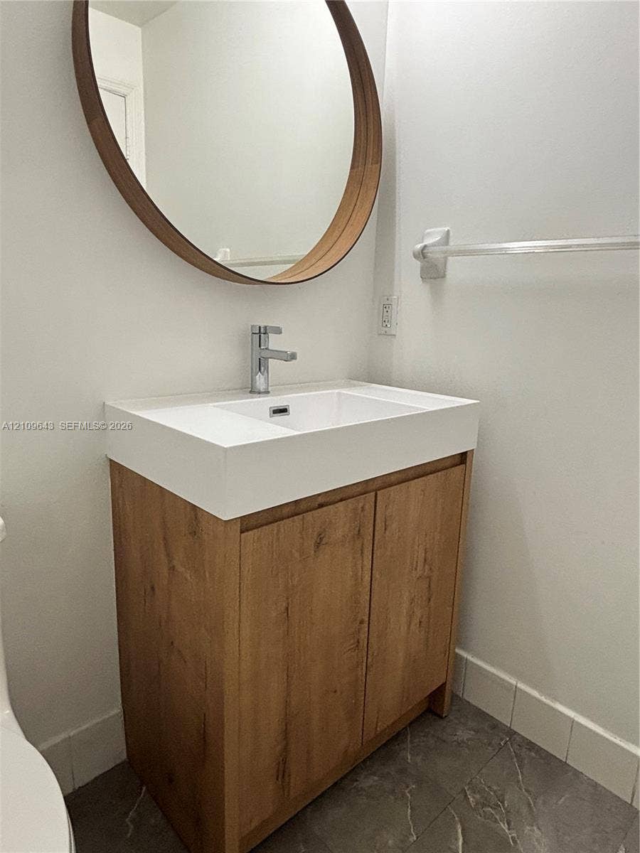 11467 NW 51st Terrace, Doral, Doral, FL 33178 Vanity featuring a wood-finish cabinet, integrated white countertop with rectangular basin, chrome single-handle faucet, and circular wall-mounted mirror with a wood frame