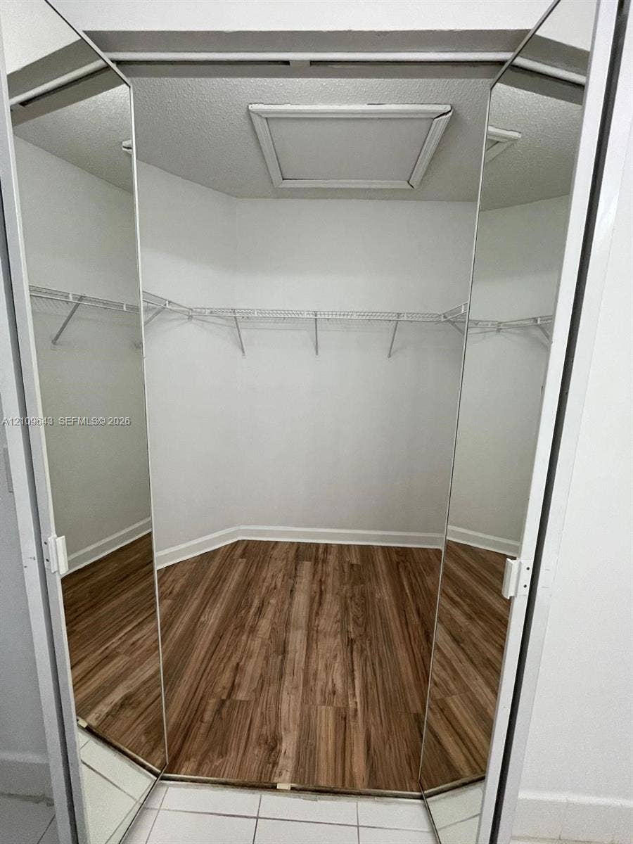 11467 NW 51st Terrace, Doral, Doral, FL 33178 Walk-in closet featuring mirrored bifold doors, wood-finish flooring, and integrated wire shelving