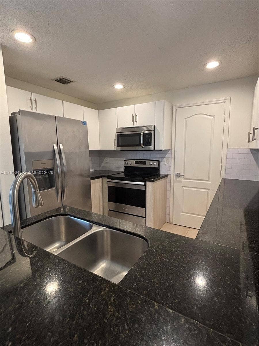 11467 NW 51st Terrace, Doral, Doral, FL 33178 Kitchen featuring dark stone countertops, stainless steel appliances, white subway tile backsplash, white upper cabinetry, and a dual-basin stainless steel sink with a high-arch faucet