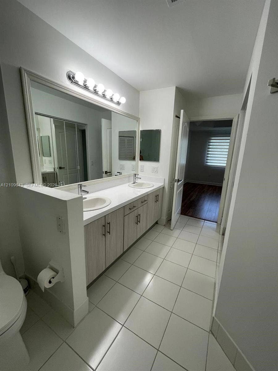 11467 NW 51st Terrace, Doral, Doral, FL 33178 Double vanity featuring light-toned cabinetry, white countertop with dual drop-in sinks, full-width wall mirror, and large-format tile flooring