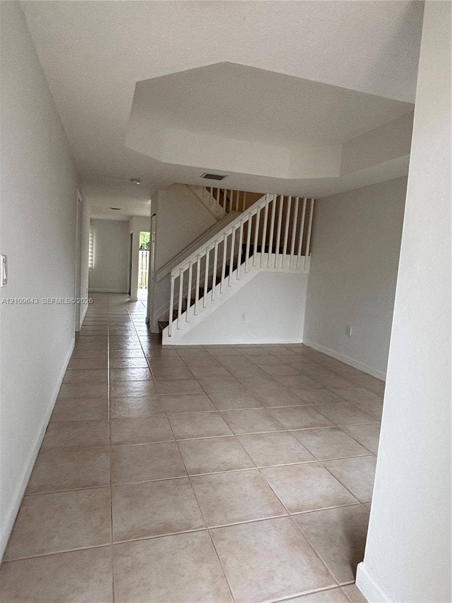 11467 NW 51st Terrace, Doral, Doral, FL 33178 Interior space featuring large-format ceramic tile flooring, a tray ceiling, and a wooden staircase with white balusters