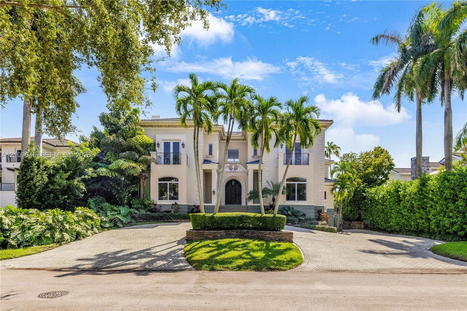 332 Costanera Road, Coral Gables, FL 33143 Two-story Mediterranean-style exterior featuring a stucco facade, arched entryway, upper-level balconies with wrought-iron railings, and a circular paved driveway