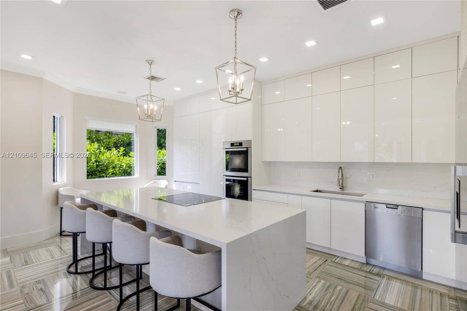 332 Costanera Road, Coral Gables, FL 33143 Modern kitchen featuring high-gloss cabinetry, stone-finish countertops, an oversized center island, built-in stainless steel appliances, and patterned tile flooring