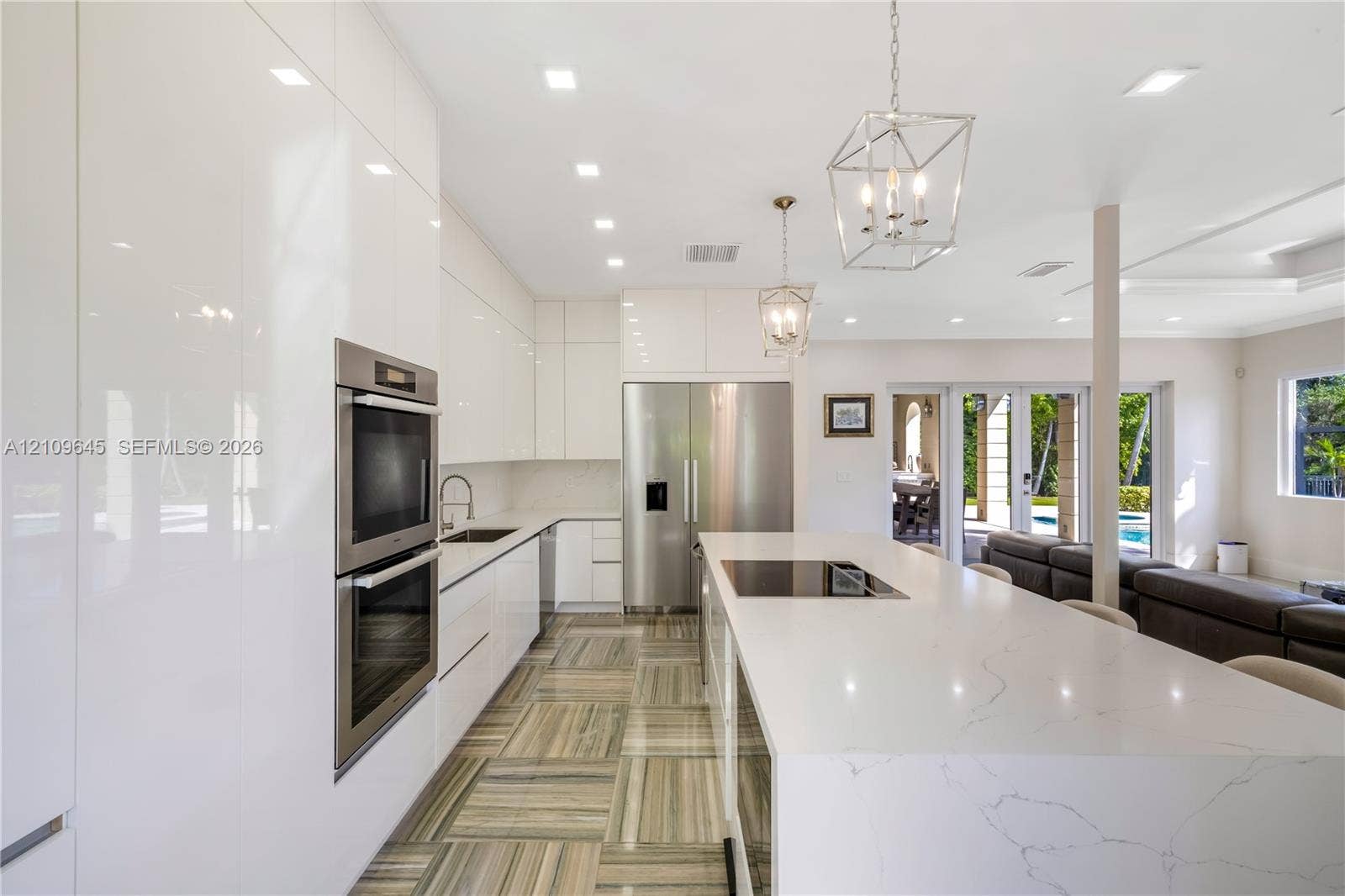 332 Costanera Road, Coral Gables, FL 33143 Kitchen featuring high-gloss cabinetry, stone-surfaced center island with integrated cooktop, built-in stainless steel double ovens, recessed lighting, and patterned tile flooring