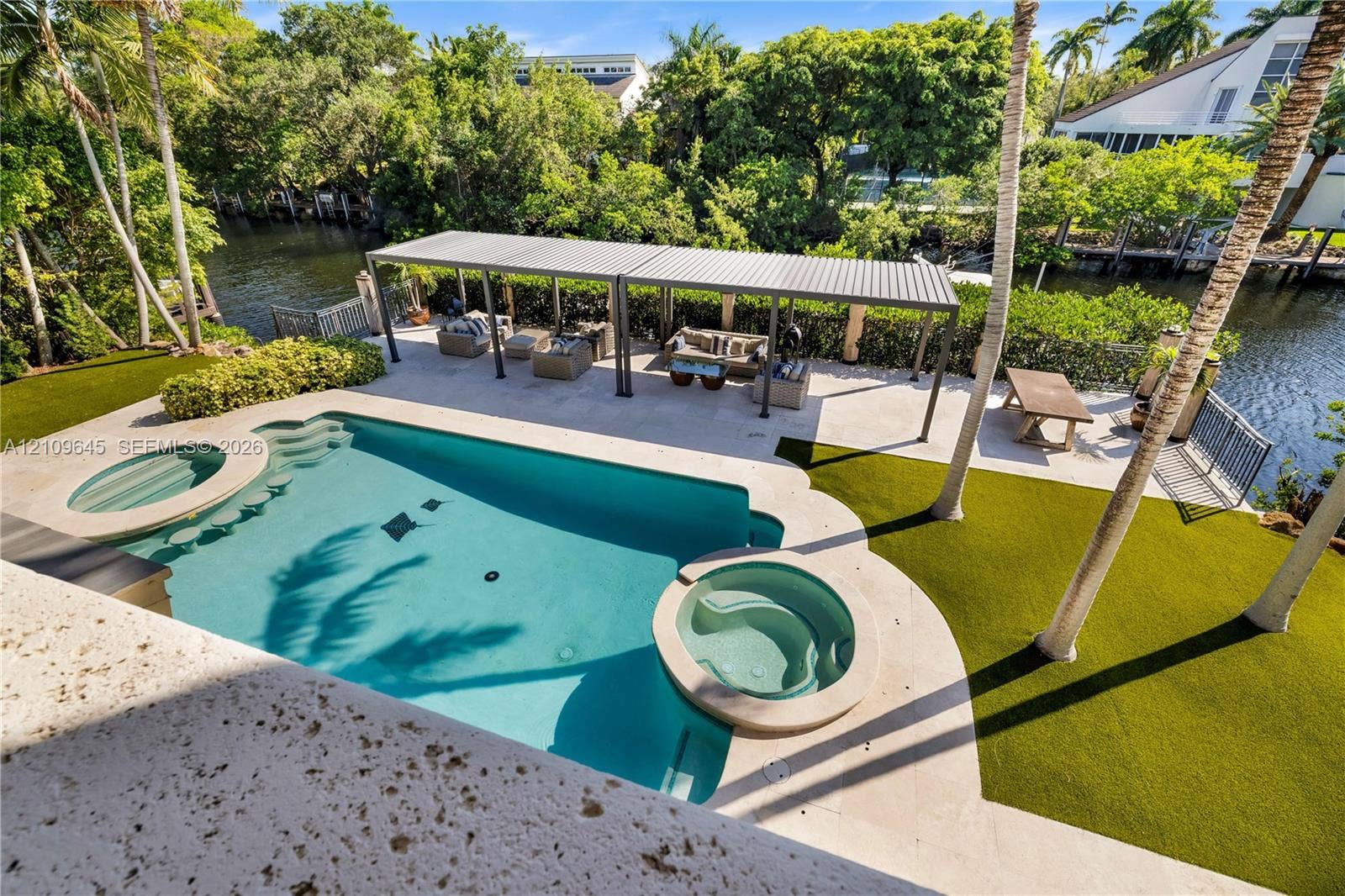 332 Costanera Road, Coral Gables, FL 33143 Waterfront backyard featuring a swimming pool with integrated spa, paved patio area, metal-frame pergola, and artificial turf lawn