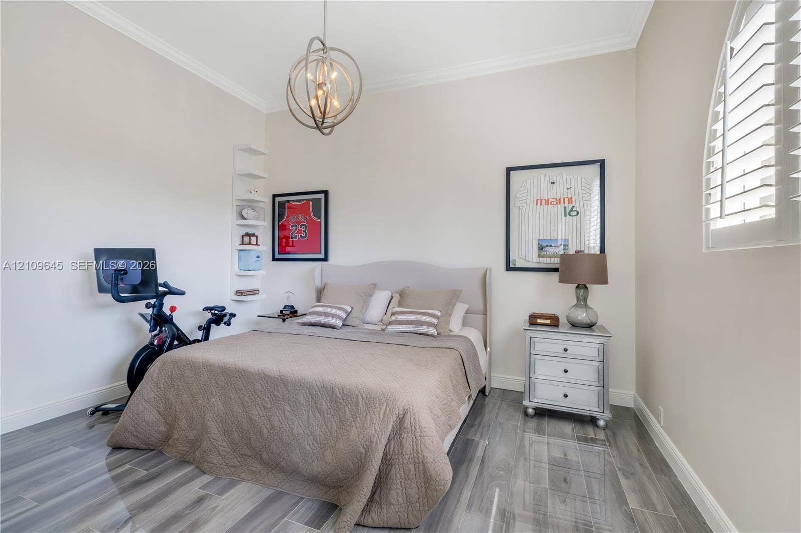 332 Costanera Road, Coral Gables, FL 33143 Room featuring wood-finish flooring, crown molding, a decorative orb chandelier, built-in shelving, and an arched window with plantation shutters